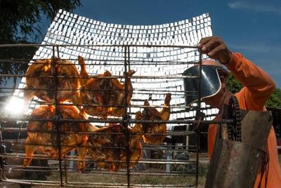 Тайский продавец уличной еды готовит курицу с помощью солнечных лучей