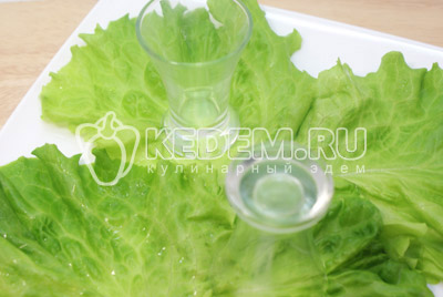 На тарелку уложить листья салата и поставить пару стаканов или стопочек для оформления