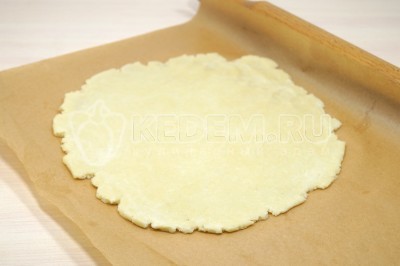 Тесто для пирога достать из холодильника и раскатать на листе пергаментам в круг диаметром чуть больше 26 сантиметров.