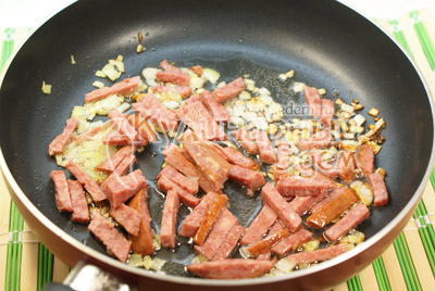 На сковороде с растительным маслом обжарить мелко нашинкованный лук и колбасу нарезанную соломкой