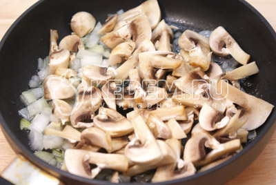 Добавить ломтиками порезанные грибы шампиньоны и обжаривать 1-2 минуты