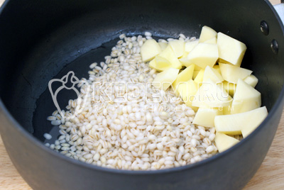 В кастрюлю сложить крупу и кубиками порезанный картофель. Залить водой и варить 5-7 минут