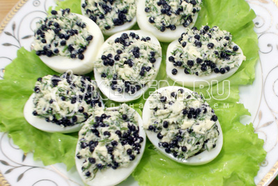 Нафаршировать половинки яичных белков начинкой и выложить на блюдо с листьями салата