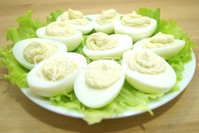 Выложить начинку в половинки белков (при помощи кулинарного мешочка). Выложить фаршированные яйца на блюдо с листьями салата.