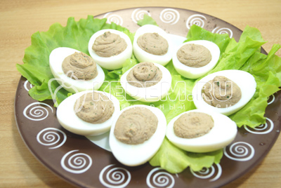 Выложить начинку в половинки белков (при помощи кулинарного мешочка). Выложить фаршированные яйца на блюдо с листьями салата.