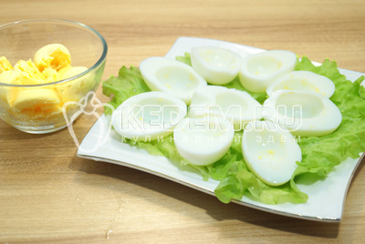 Разрезать на половинки, белки выложить на блюдо с листьями салата, желтки выложить в миску.