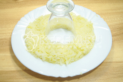 На плоское блюдо поставить перевернутый стакан, вокруг стакана выложит слой тертого картофеля, немного посолить. Смазать майонезом.
