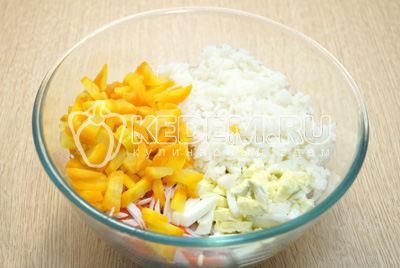 В миску с кальмарами добавить соломкой нарезанный крабовые палочки, нарезанные яйца, морковь и отварной рис.