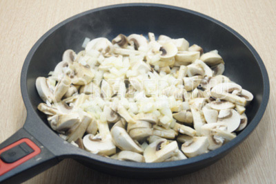 Мелко нашинкованный лук и нарезанные грибы обжарить на сковороде с растительным маслом, 2-3 минуты помешивая.
