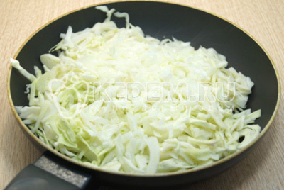 В сковороду с растительным маслом выложить нашинкованную капусту и мелко нашинкованный лук.