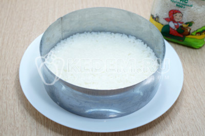 На блюдо установить сервировочное кольцо и выложить половину риса нижним слоем.