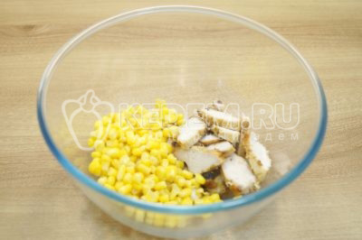 В миску выложить 100 г консервированной кукурузы и нарезанное куриное филе.