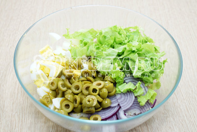Добавить в миску оливки и нарезанные листья салата.
