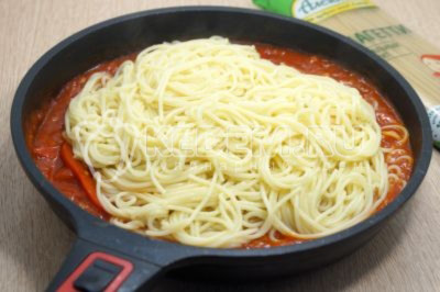 Слить воду с готовых спагетти. Добавить горячие спагетти в сковороду с соусом и сразу перемешать.