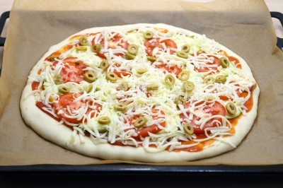 Добавить сверху тертый сыр и колечки оливок. Переложить пиццу на противень.