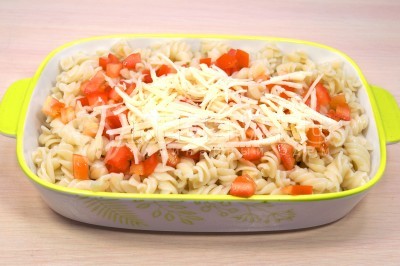 Добавить кубками нарезанный помидор и половину тертого сыра, перемешать с макаронами.