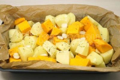 Выложить тыкву с картошкой в форму для запекания в духовке и разровнять. Добавить 3-4 нарезанных зубчика чеснока.