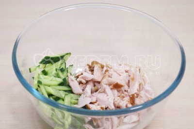 В большую глубокую миску выложить нарезанный соломкой свежий огурец и нарезанное соломкой копченое куриное филе.