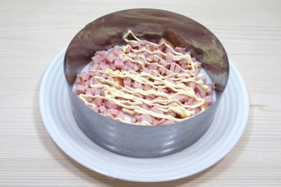 На блюдо установить сервировочное кольцо. Выложить слой ветчины и смазать майонезом.